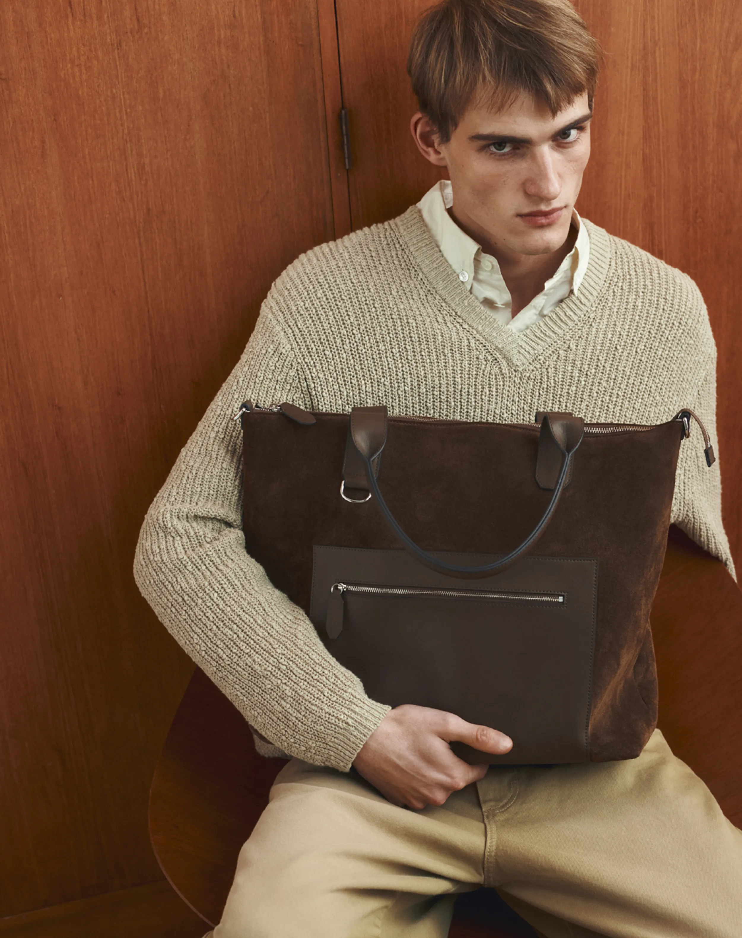 Young man in a sweater holding a brown tote bag.