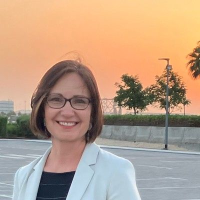 Smiling woman in a blazer with sunset background.