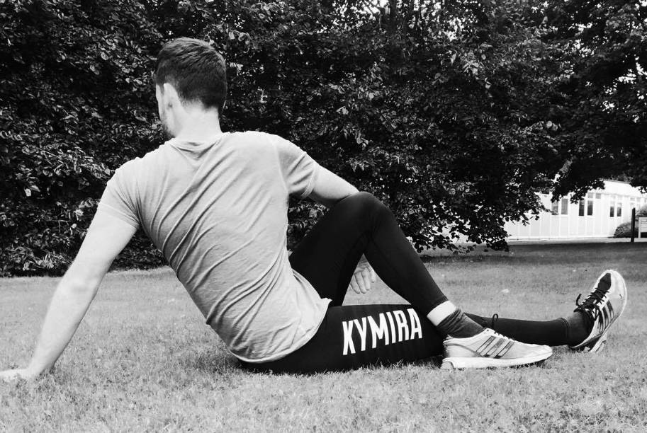 A man wearing KYMIRA kit stretches out on the grass.