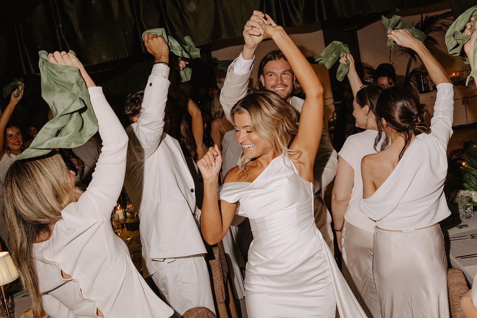 People dancing at a celebration, wearing elegant outfits and holding colorful scarves.