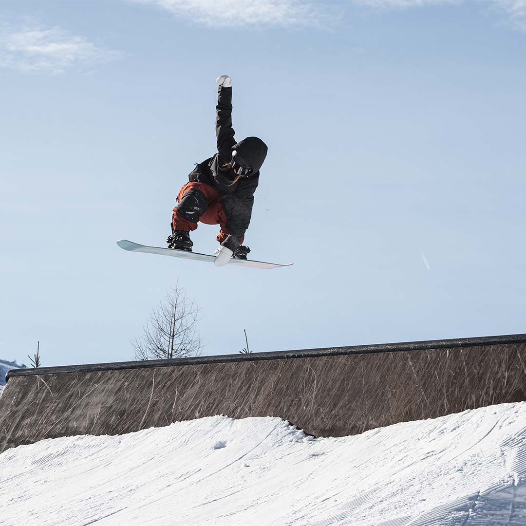 An athlete completes a jump on their snowboard, and is about to land and continue their descent.