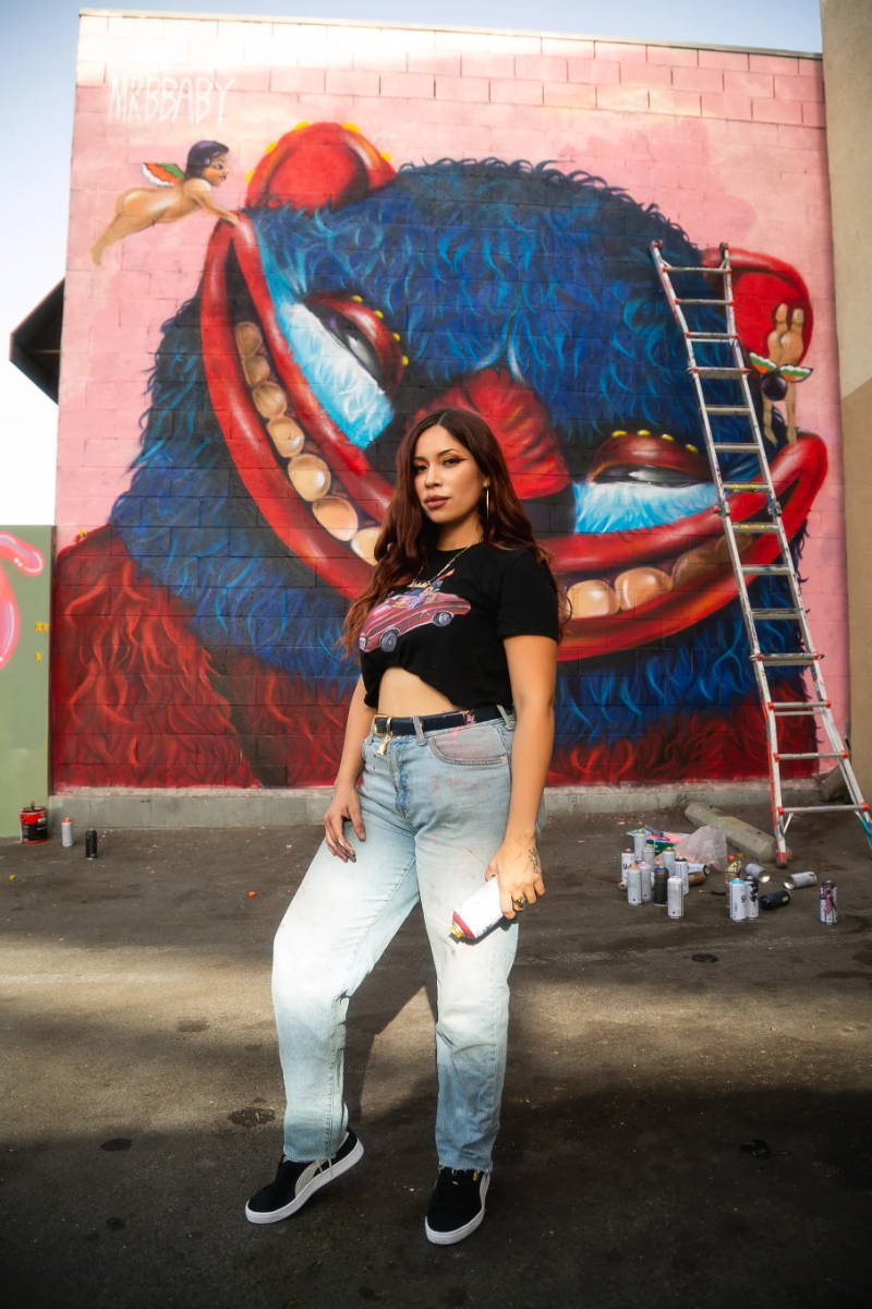 woman holding spray paint in front of mural wearing puma suede shoes