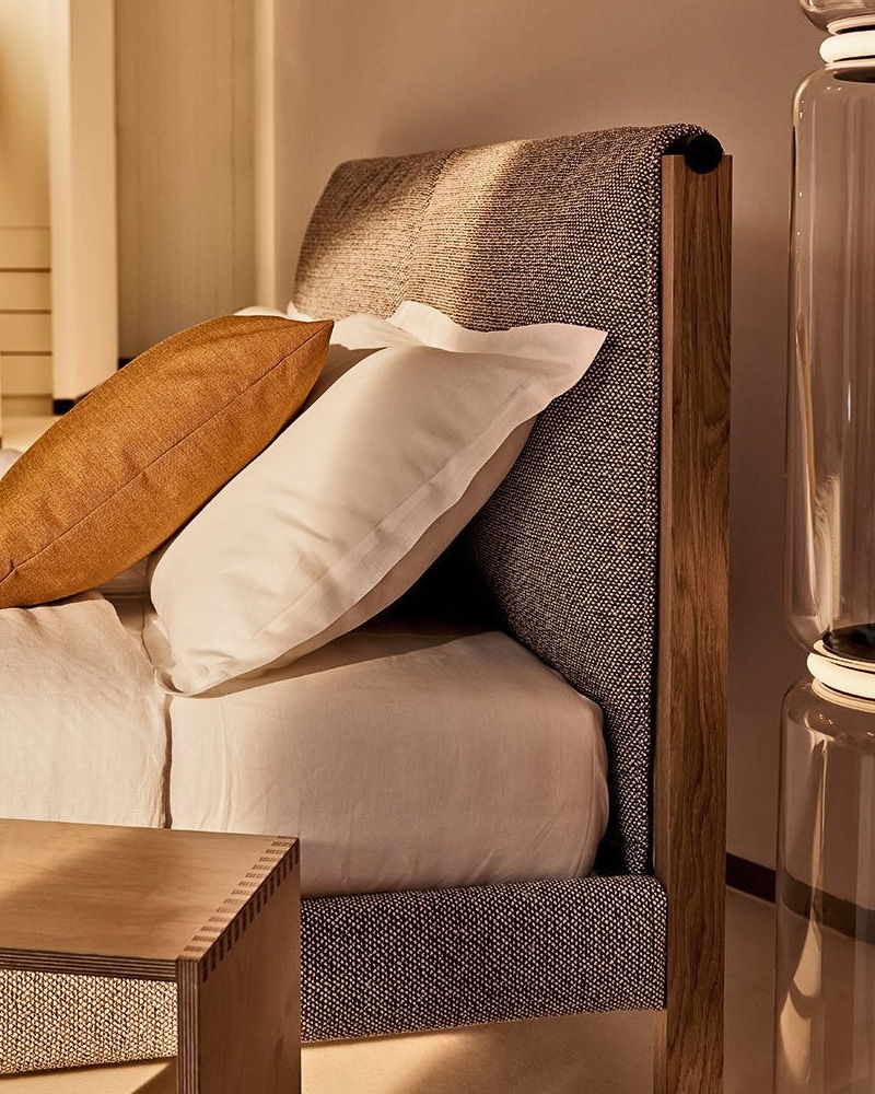 Cozy Zanotta bed with pillows and a decorative cushion, warm lighting.