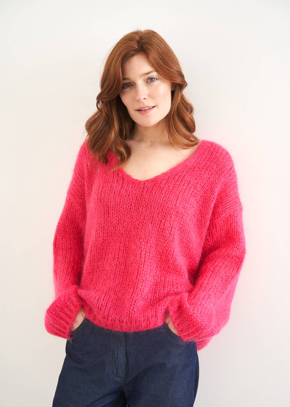 A model wearing a pink knitted v neck sweater with blue chambray jeans