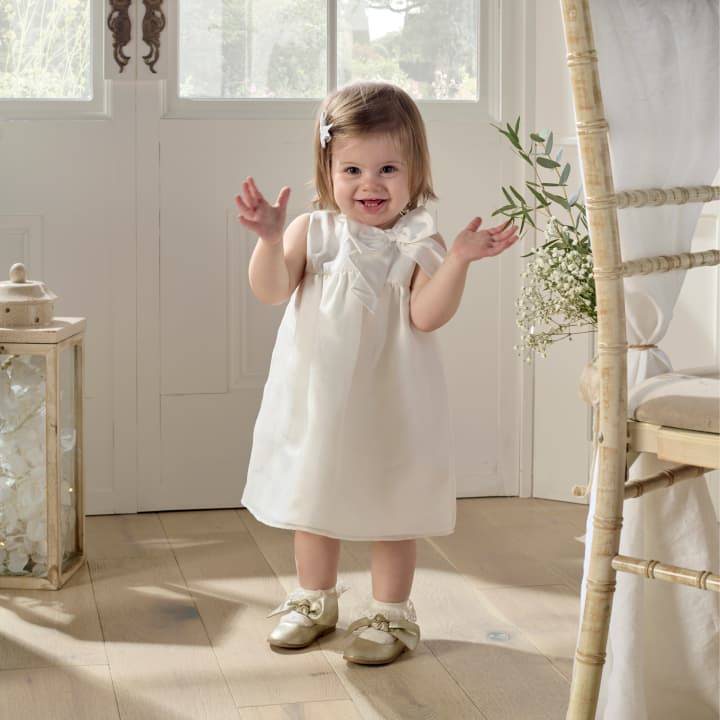 A little girl in a smart white dress stands smiling in a wedding reception room.
