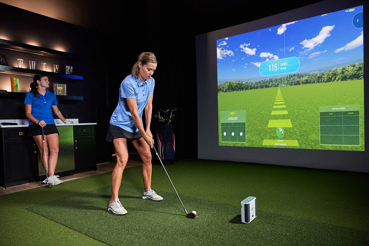 Two women in a home golf simulator with one getting ready to swing in front of a SkyTrak+ golf launch monitor