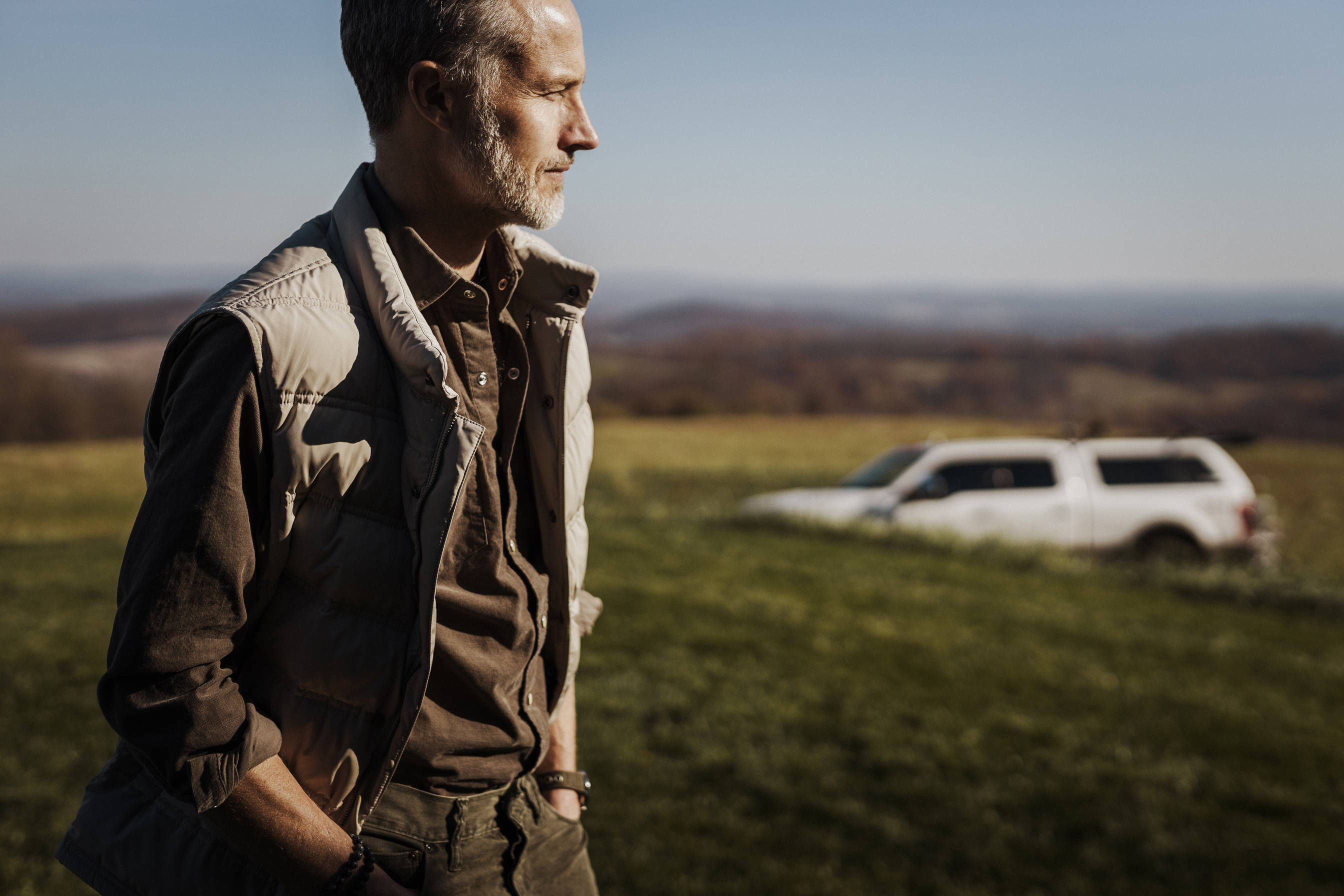 A man looking off into the distance wearing a vest and a corduroy shirt.