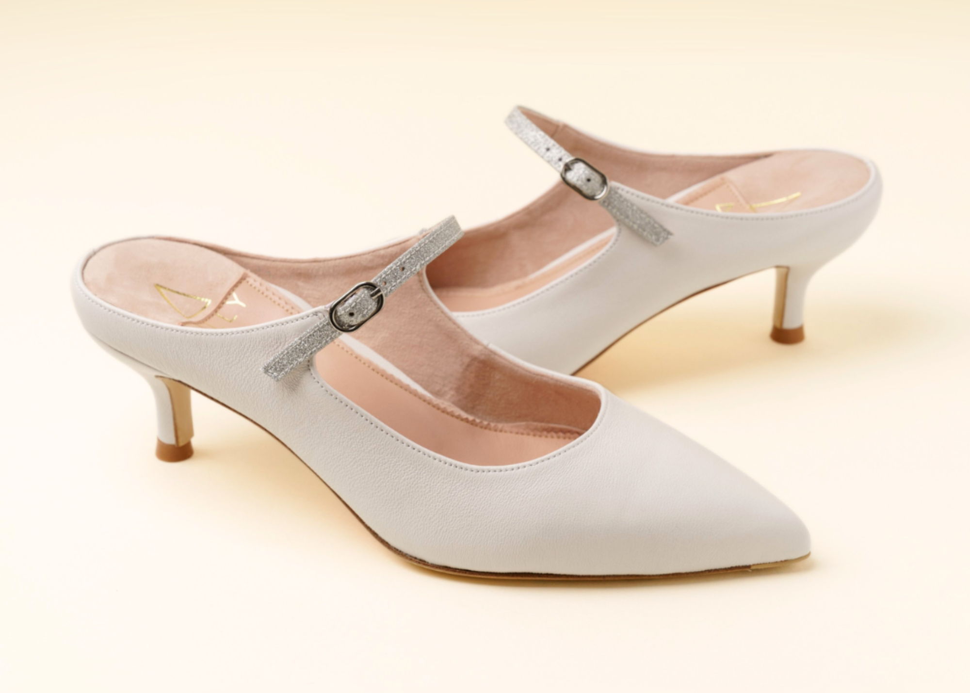 A pair of elegant white heeled mules with a strap.