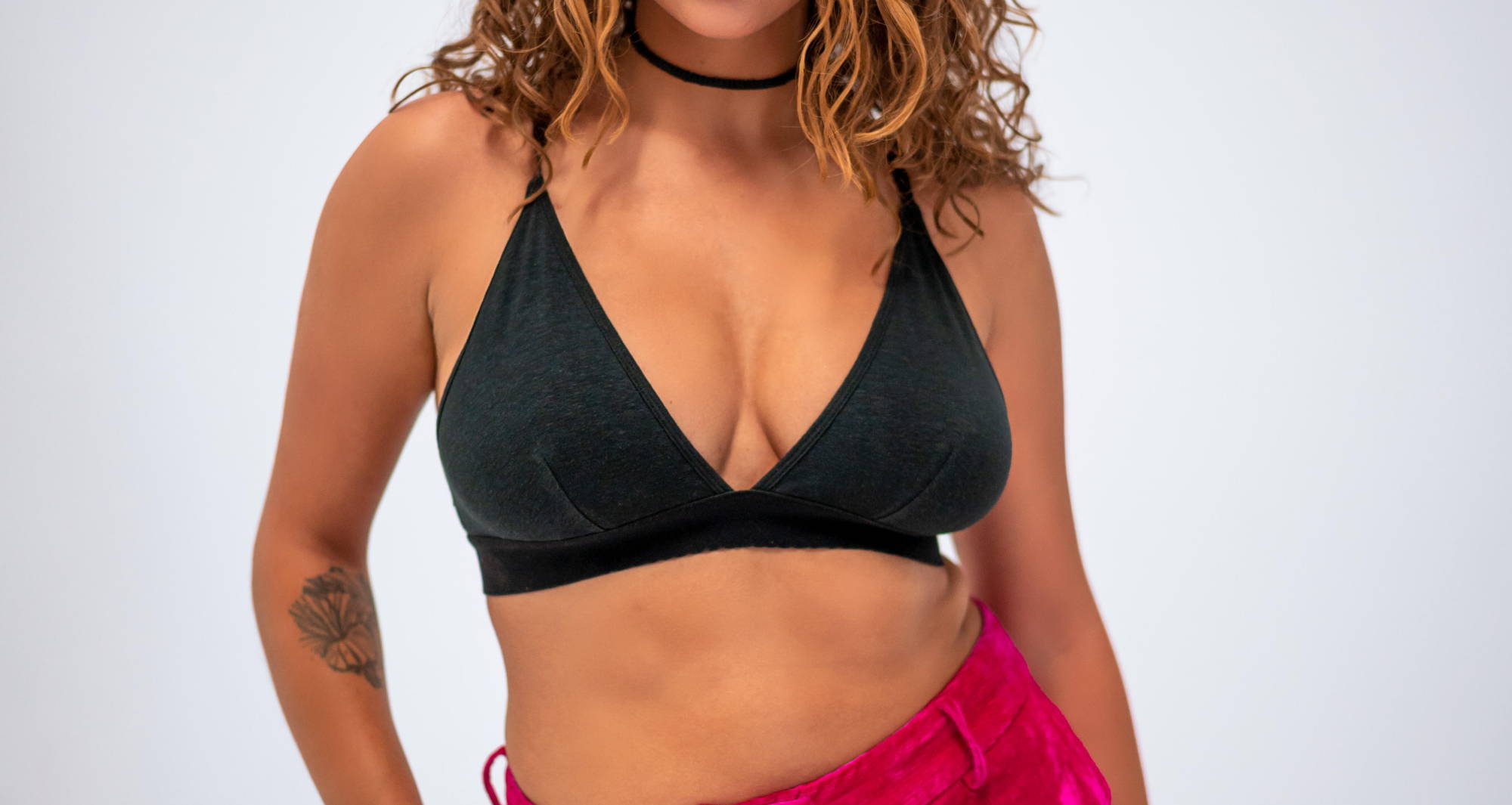 Woman with curly hair wearing a black bralette and choker necklace.
