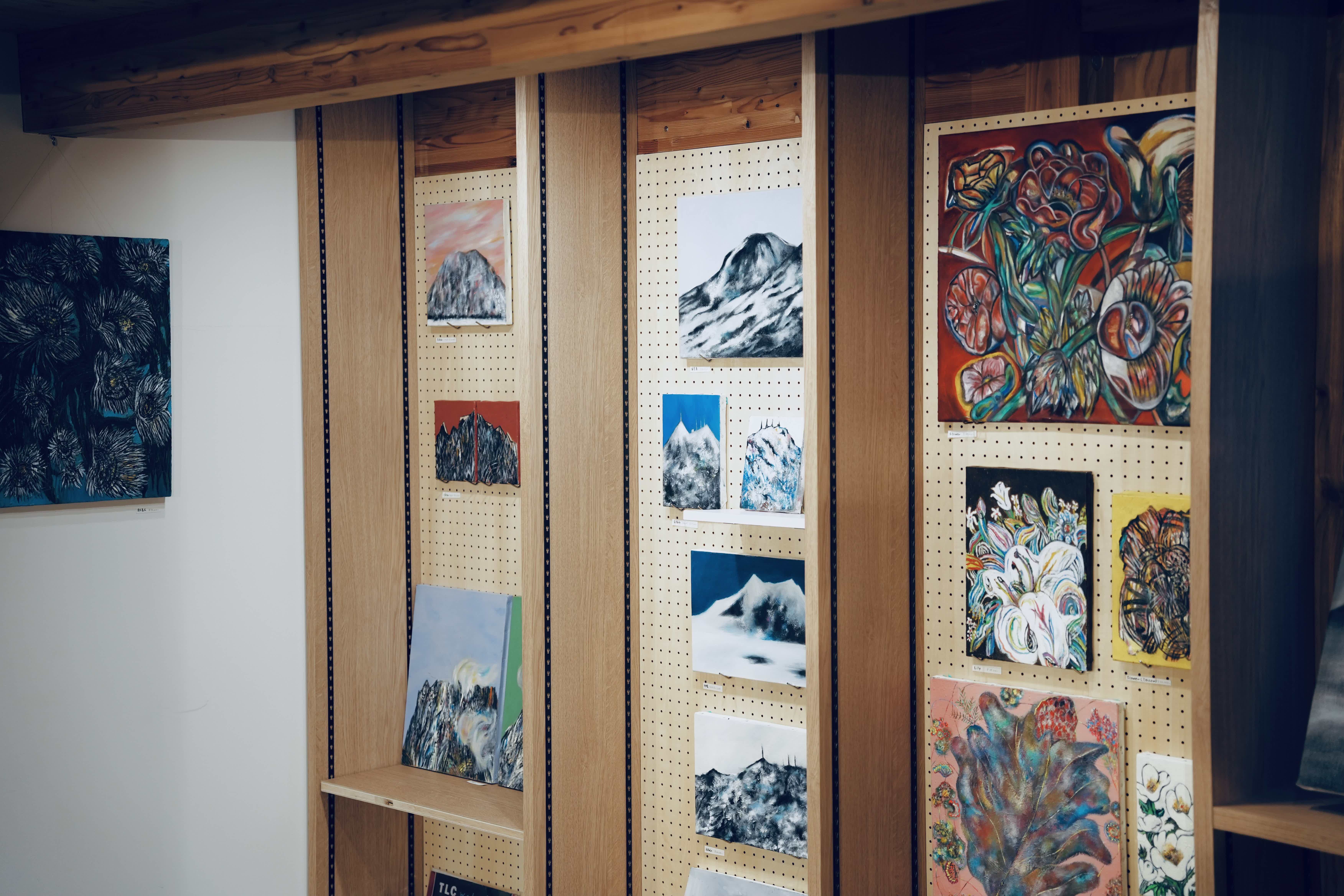 Artworks displayed on wooden shelves in a gallery setting.
