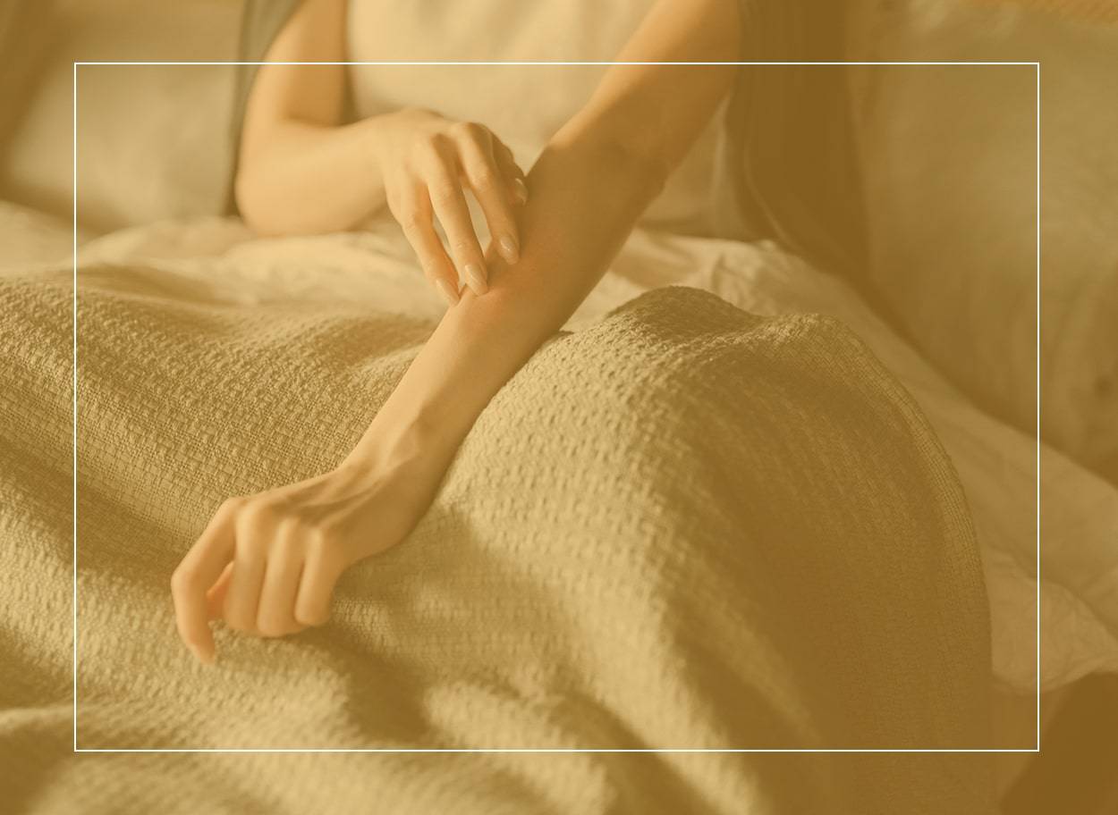 Une femme au lit se démange le bras, peut-être à cause d’une allergie aux acariens