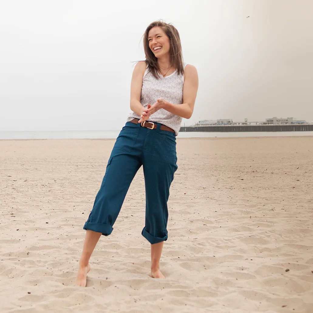 Smiling woman in casual outfit standing on a sandy beach.