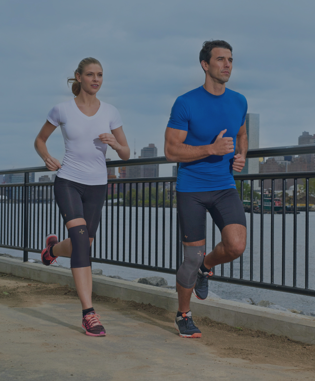 Two people jogging along a river path wearing Tommie Copper compression