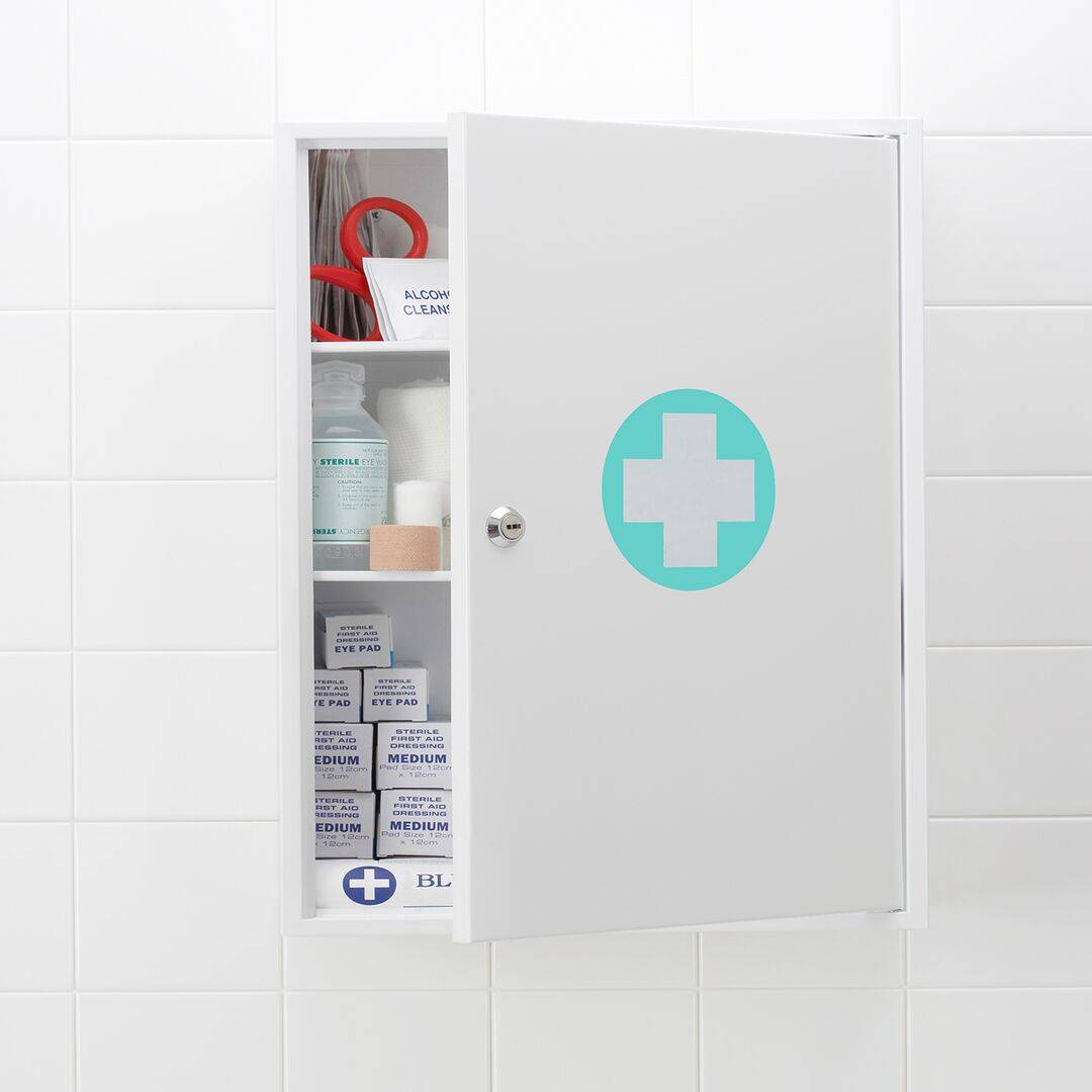 Skrinka v kúpeľni s polootvorenými dverami, na ktorých sa nachádza biely kríž v zelenom kruhu, symbolizujúci úložný priestor pre lieky
