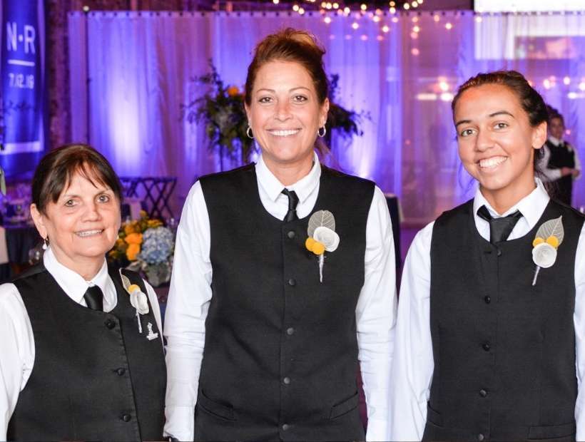 Three female caterers at event wearing classic black and white uniforms