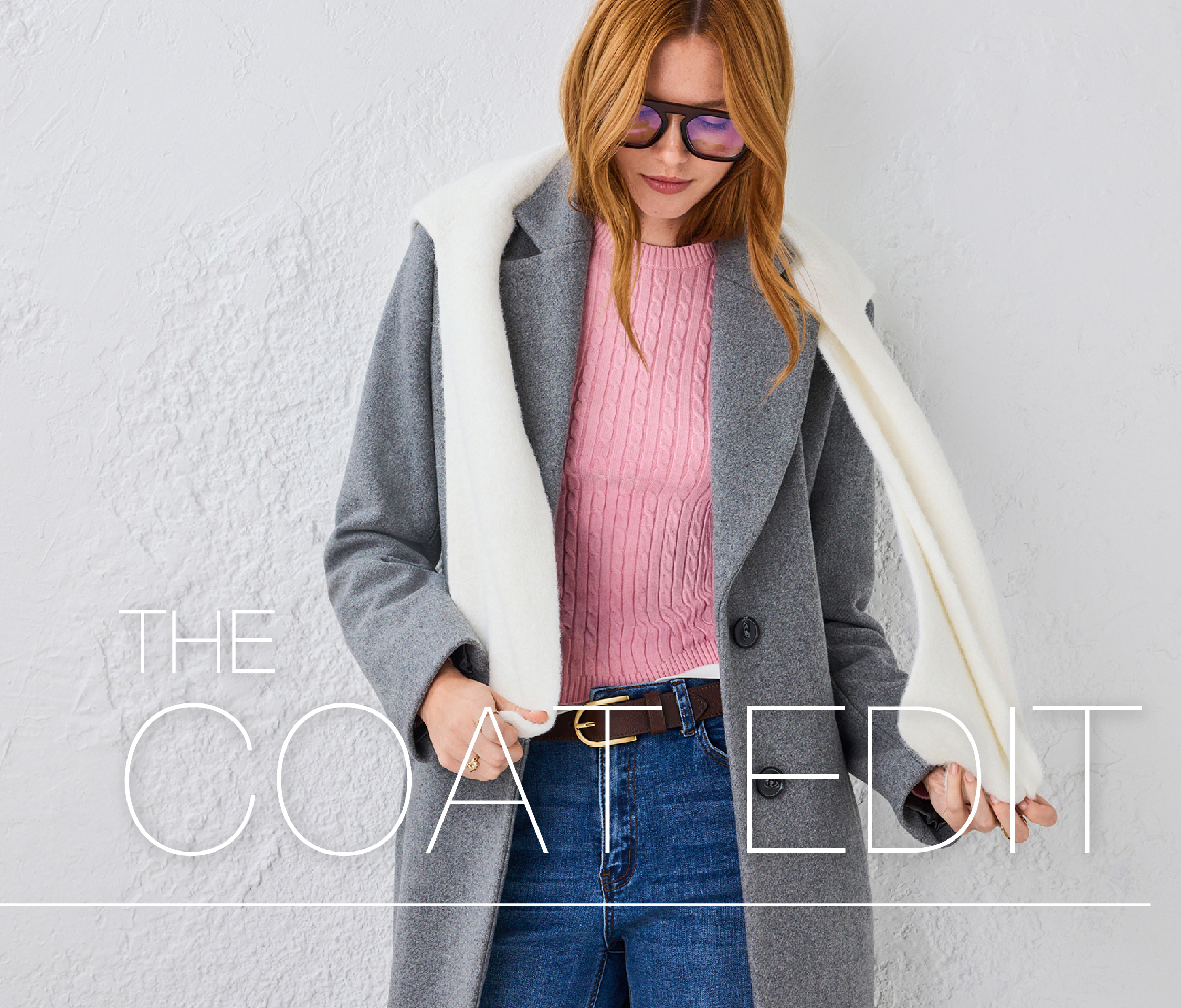 Woman wearing a gray coat and pink sweater, holding a white scarf.