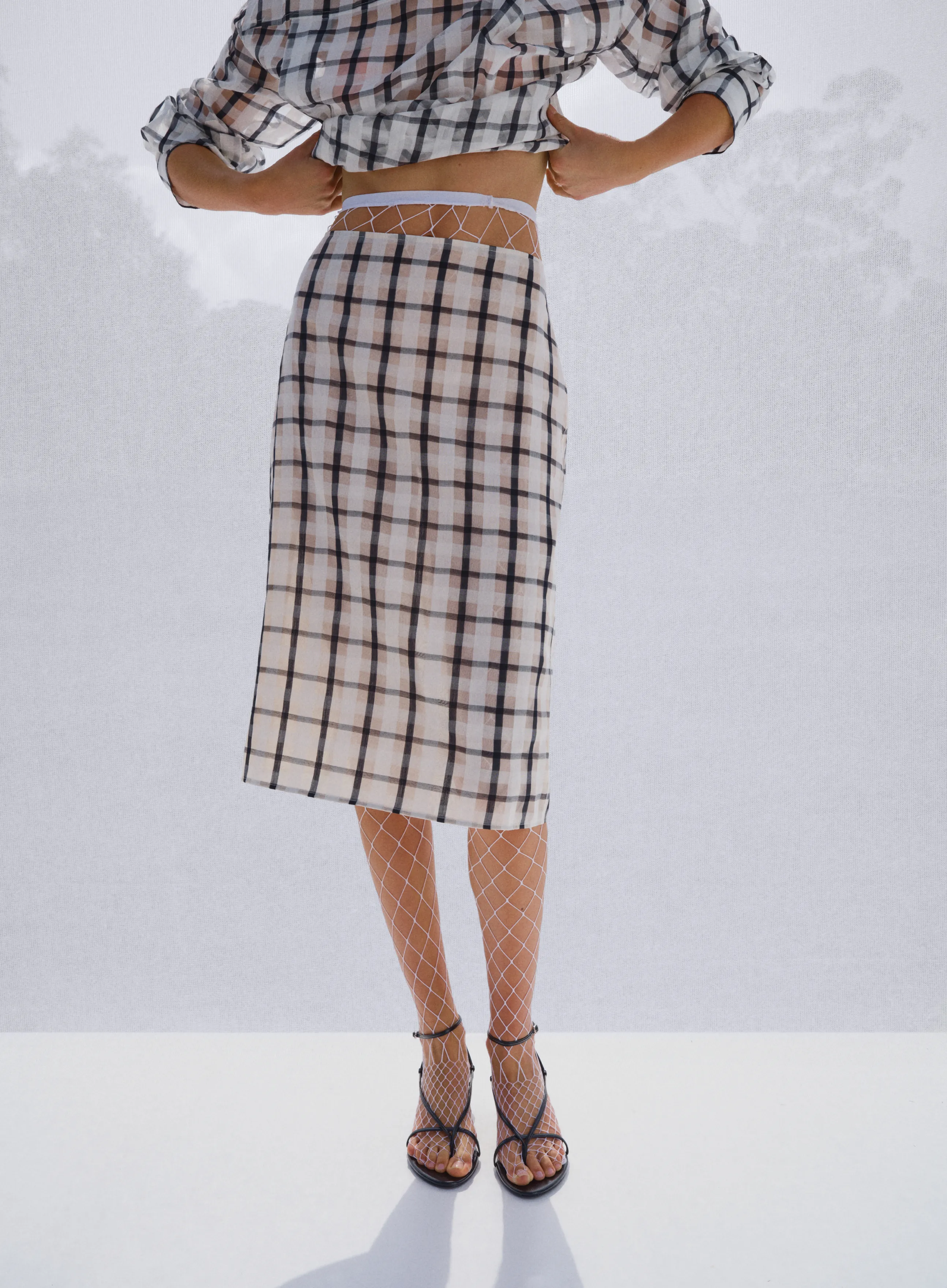 Woman wearing a checkered crop top and skirt, standing with hands on hips.