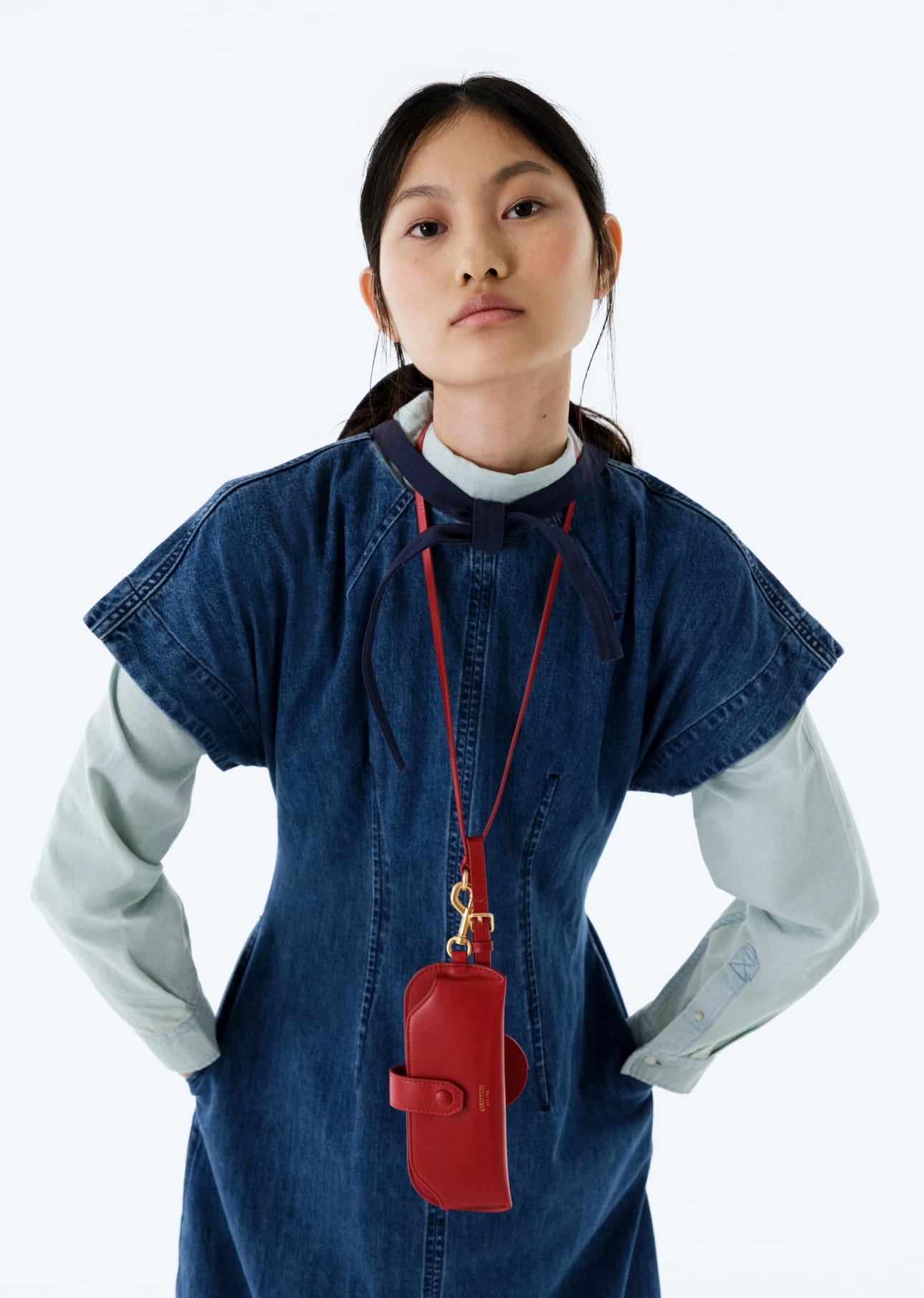 A person wearing a denim dress with a red accessory around the neck.
