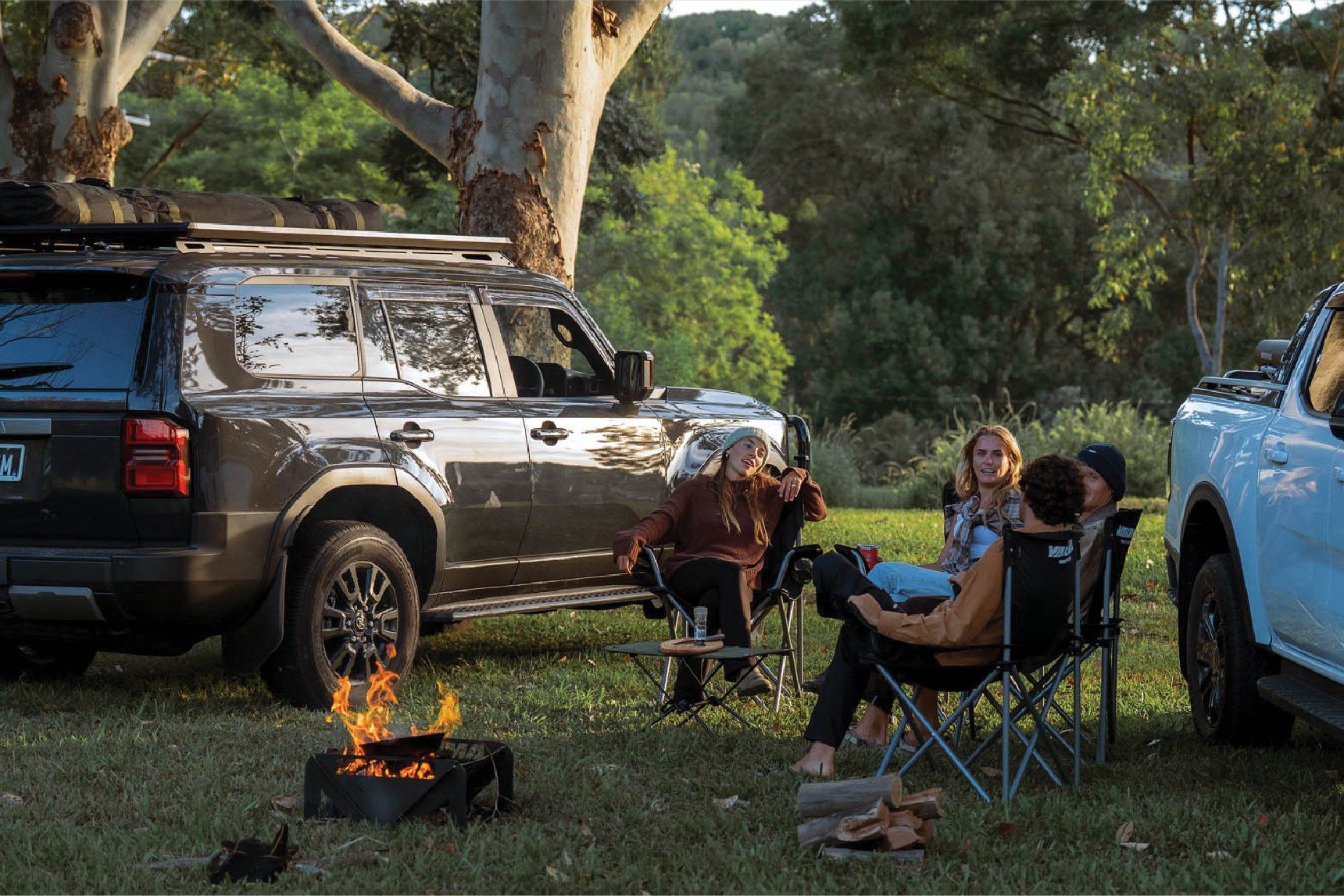 People camping outdoors around a fire with vehicles fitted with RuggedLine HD and LockNLoad Platform