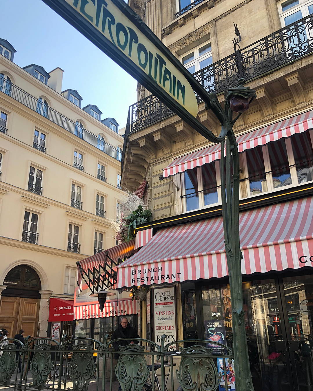 The Metropolitain sign in Paris with a cafe in the background.