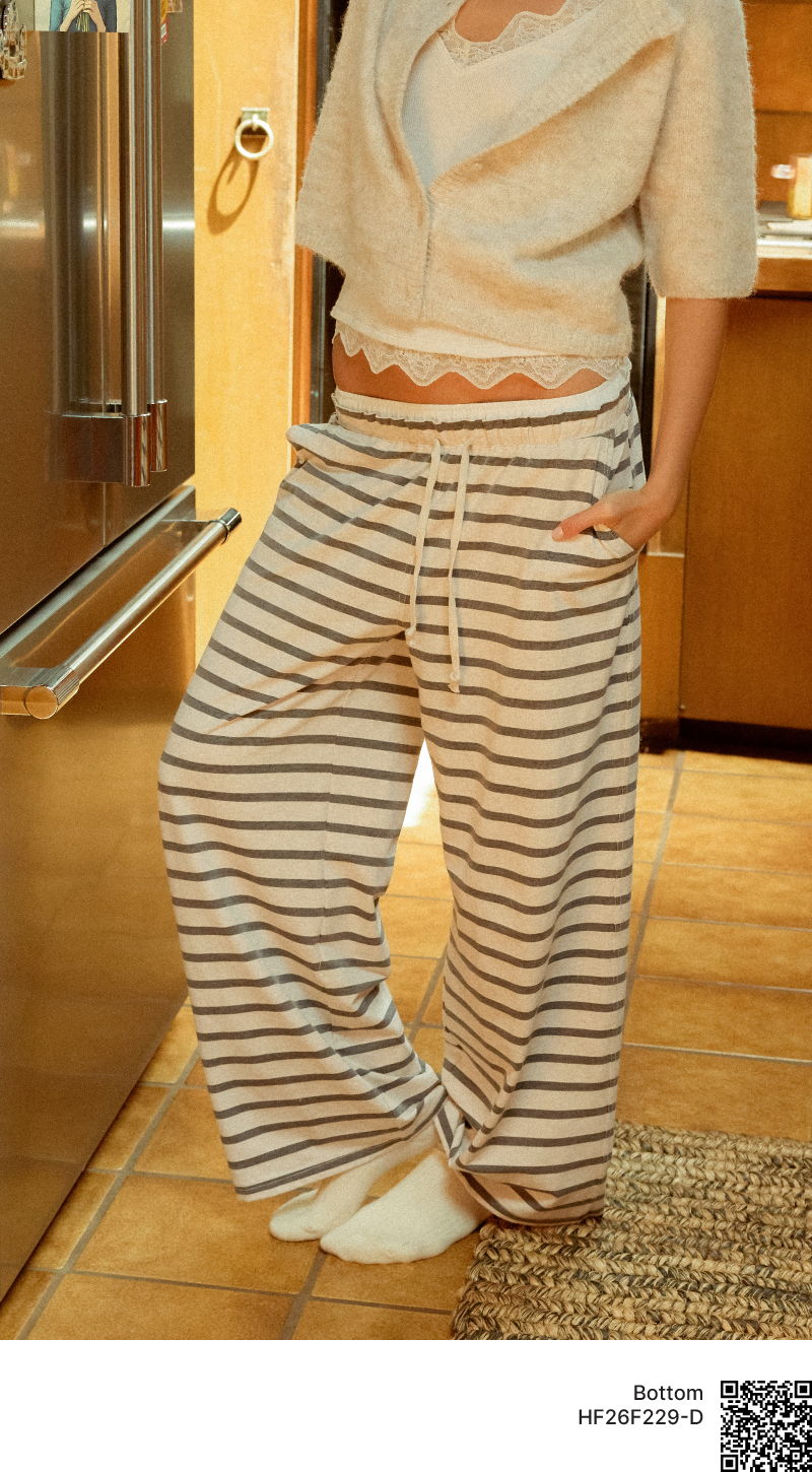 Person wearing striped pajama pants and a light sweater in a kitchen.