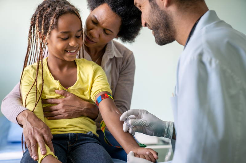 Ein Mädchen sitzt auf dem Schoß seiner Mutter und schaut zu, wie der Arzt eine Blutprobe aus ihrem Arm nimmt, um einen Allergietest durchzuführen