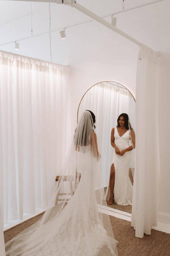 Bride trying on the Grace Loves Lace Lumi gown and Henri veil in the sheer curtain white dressing room