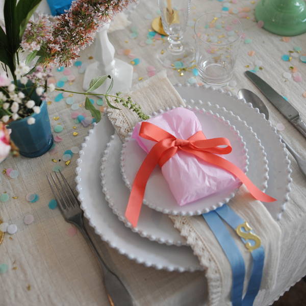A place setting with a gift wrapped in pale pink Rico Design tissue paper and tied with a fluro pink grosgrain ribbon.
