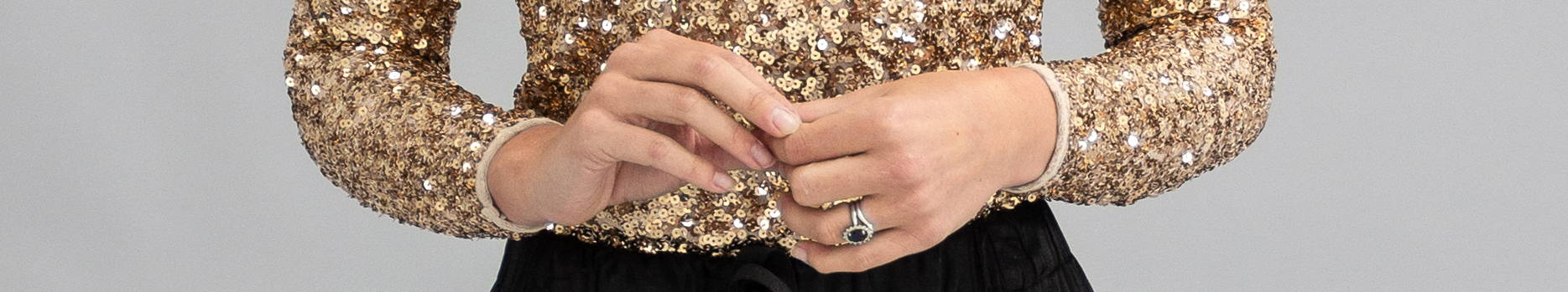 A close up of a models hands - wearing a gold sparkly long sleeved top aand gold gem ring
