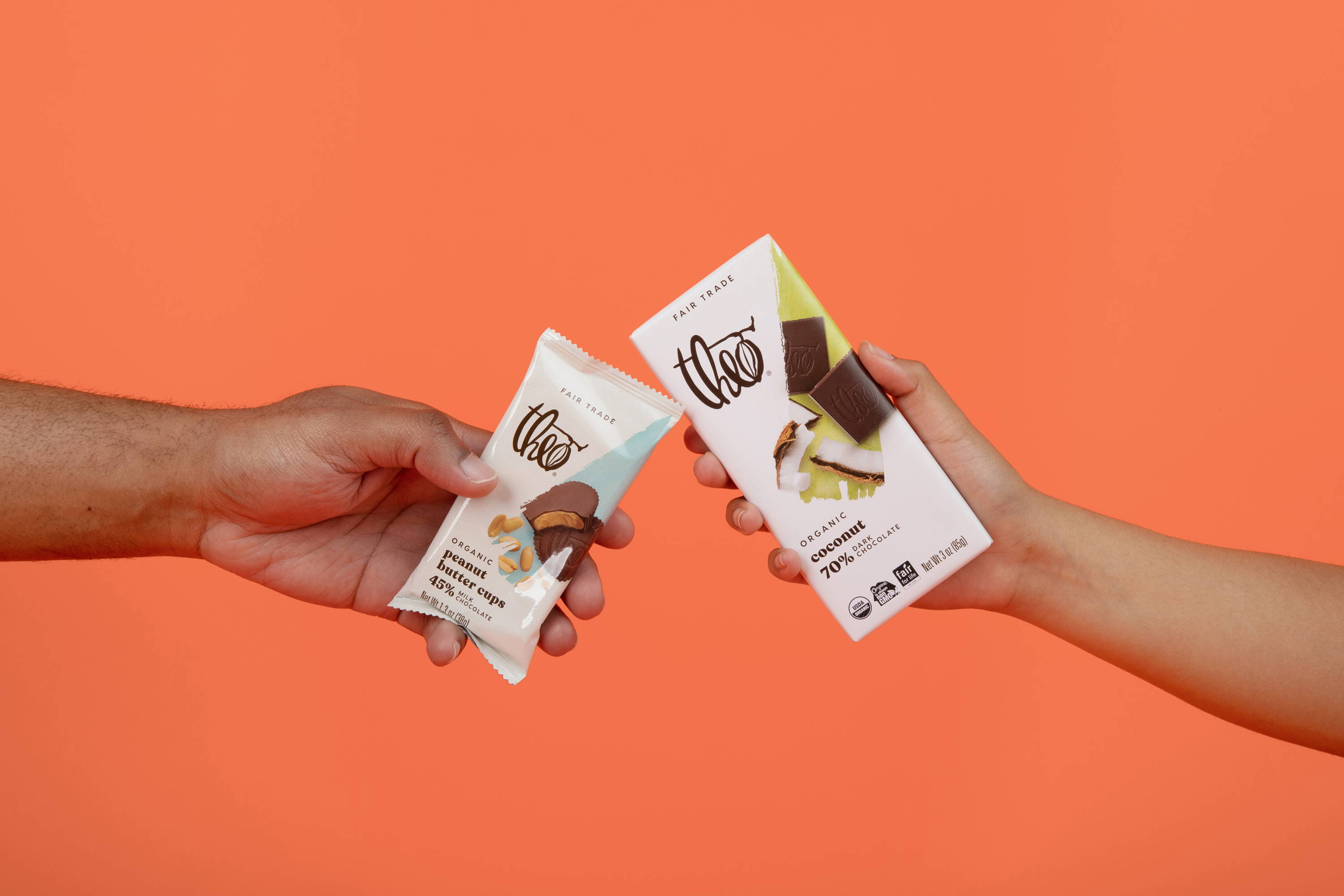 Two hands reaching out with chocolate treats in packaging against an orange background.