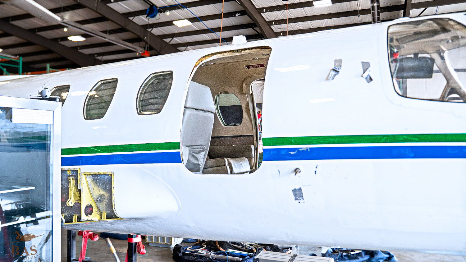 Aircraft door open in a hangar, showing interior seating and cockpit area.