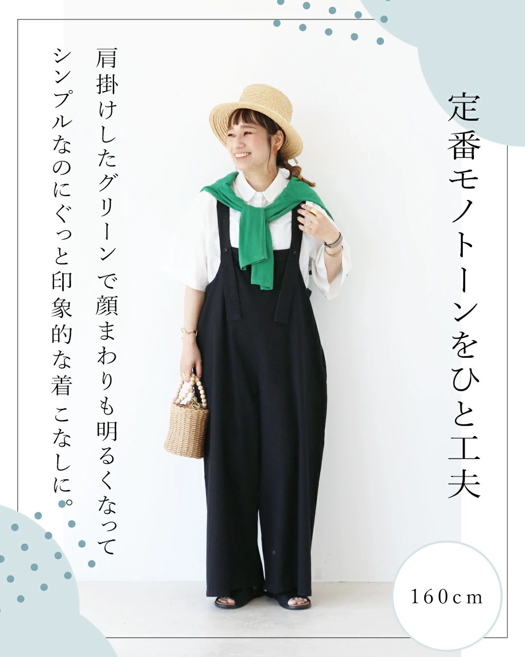 Woman wearing black overalls and green sweater, styled with a hat.