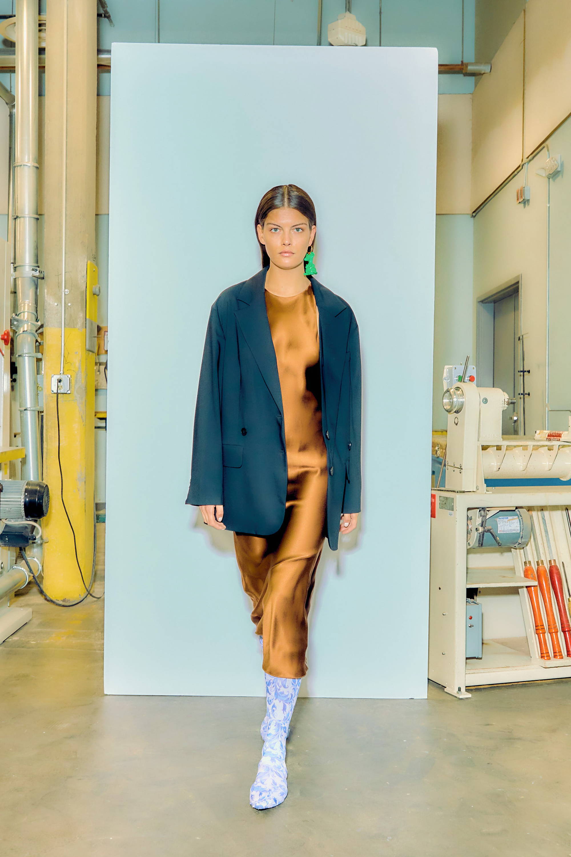 Model wearing a brown dress and black coat in a studio setting.