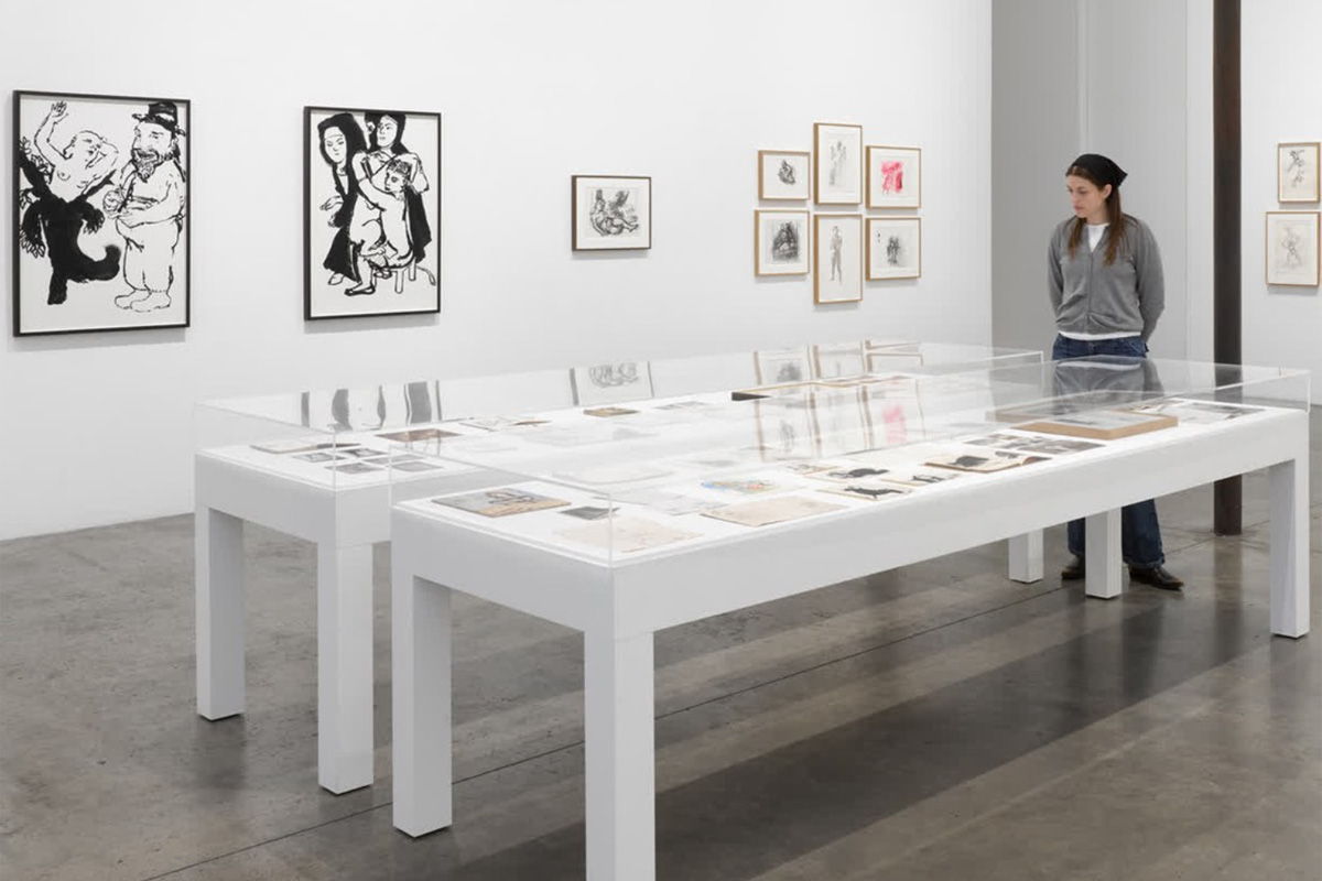 A person observing art in a contemporary gallery with white tables and framed artworks.