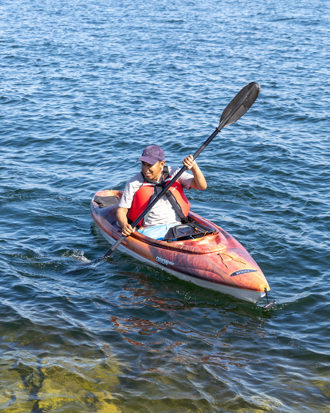 Person kayaking on a calm body of water, wearing a life jacket.