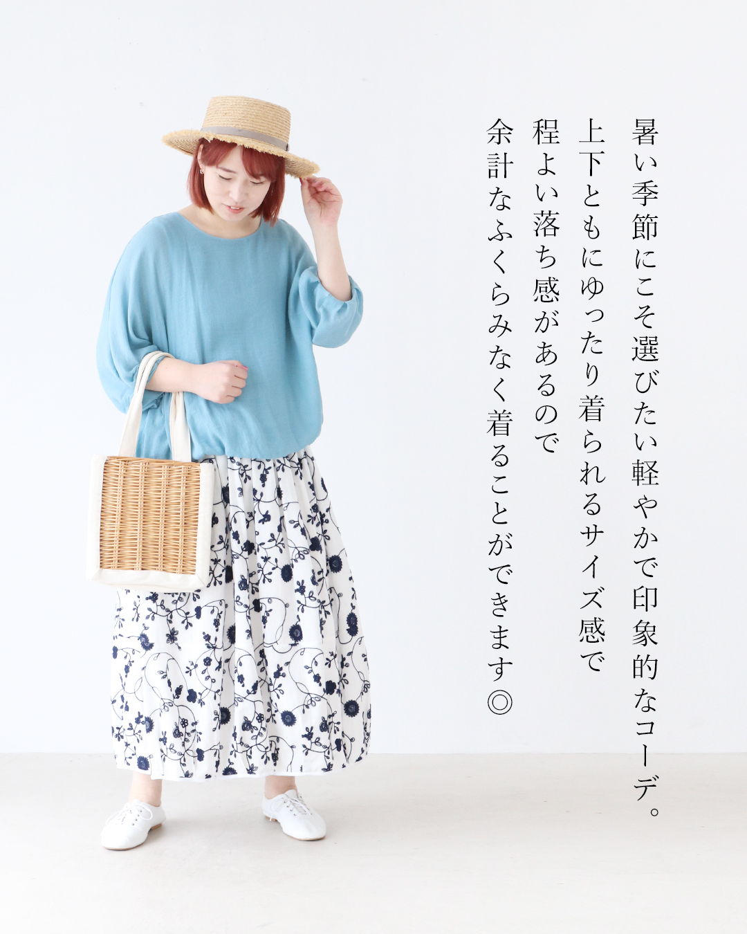 A woman in a blue top and floral skirt, wearing a straw hat.