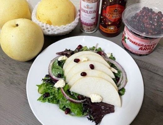 A plate of salad with sliced pear, greens, and toppings beside fruits and condiments.