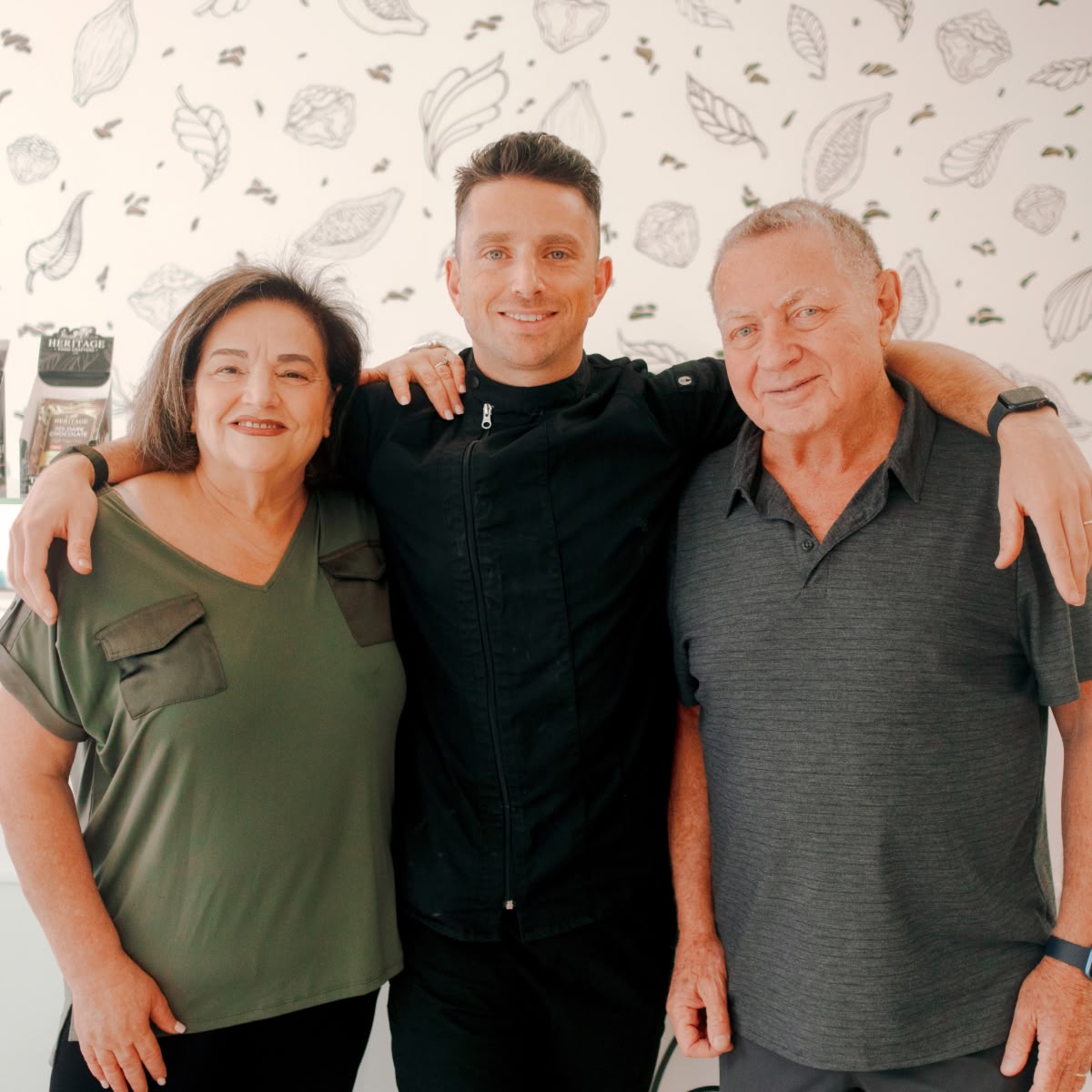 Three people posing together, smiling in front of a patterned background.