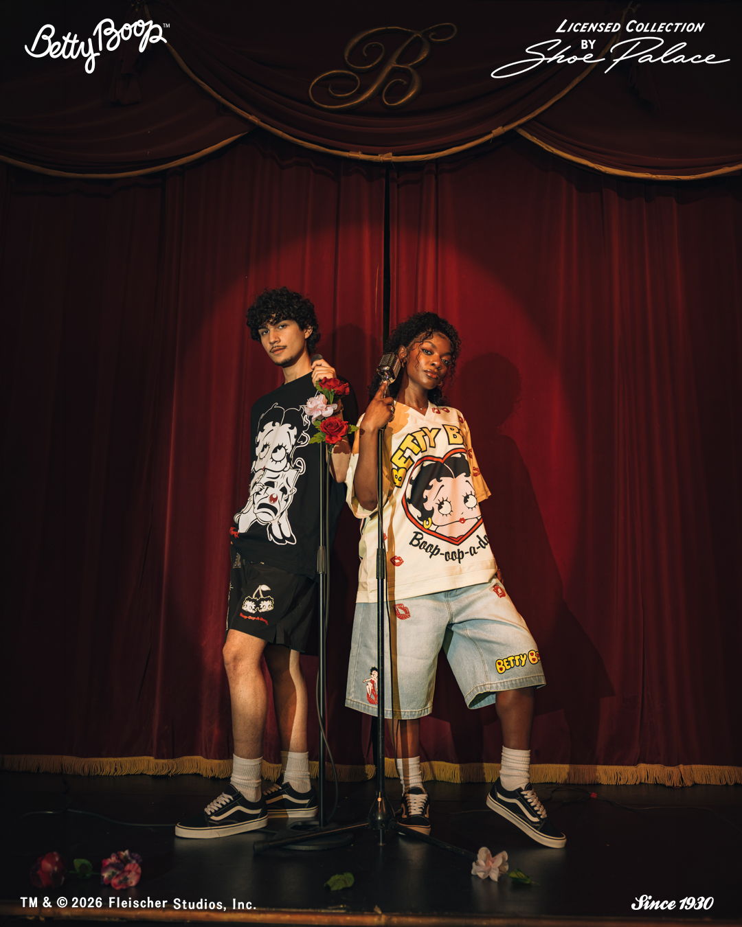 Two models posing on stage in stylish outfits with a curtain backdrop.