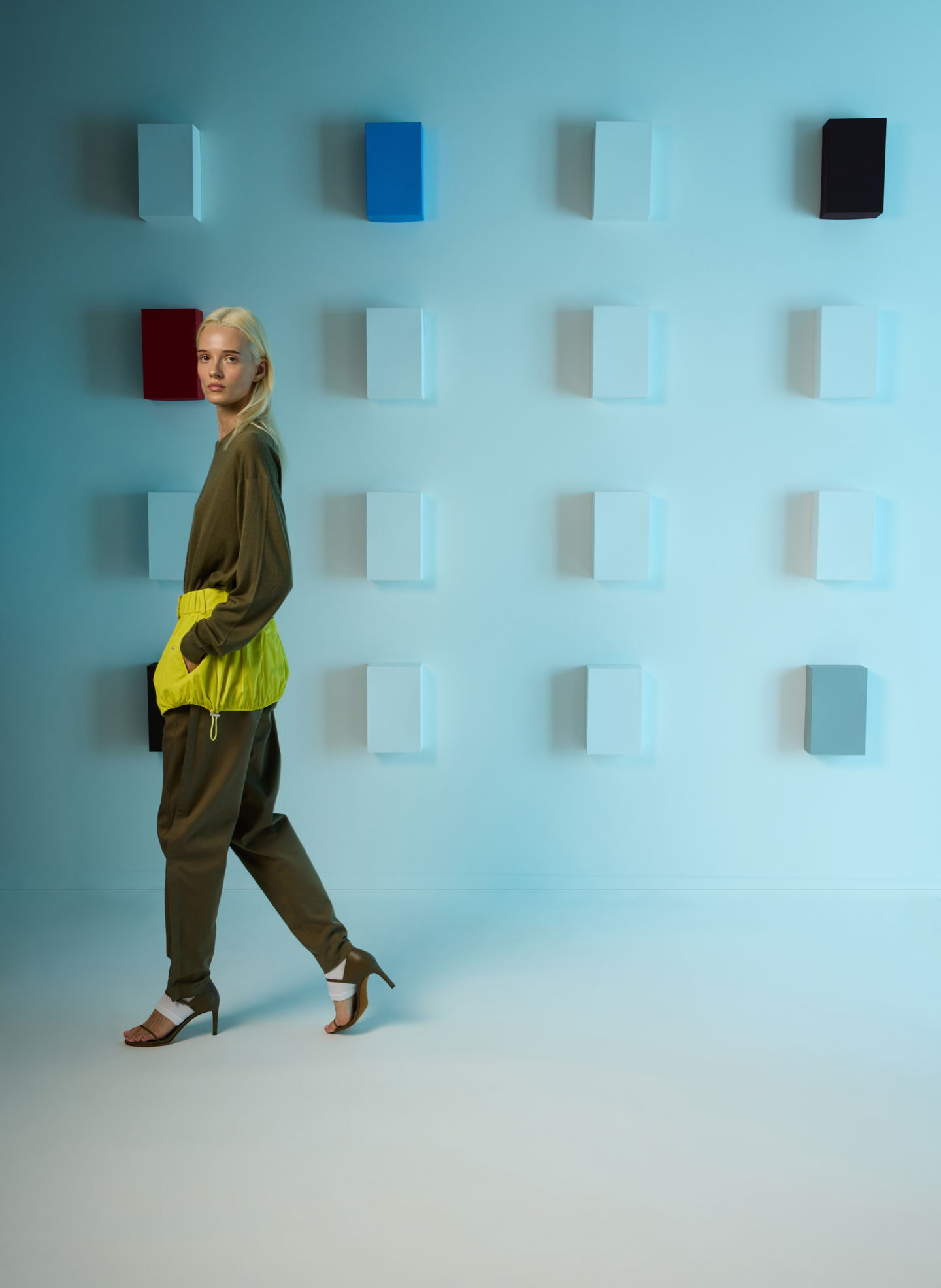 Model wearing green outfit with yellow accents against a minimalist background.