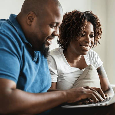 A couple smiling while using a laptop together at home.