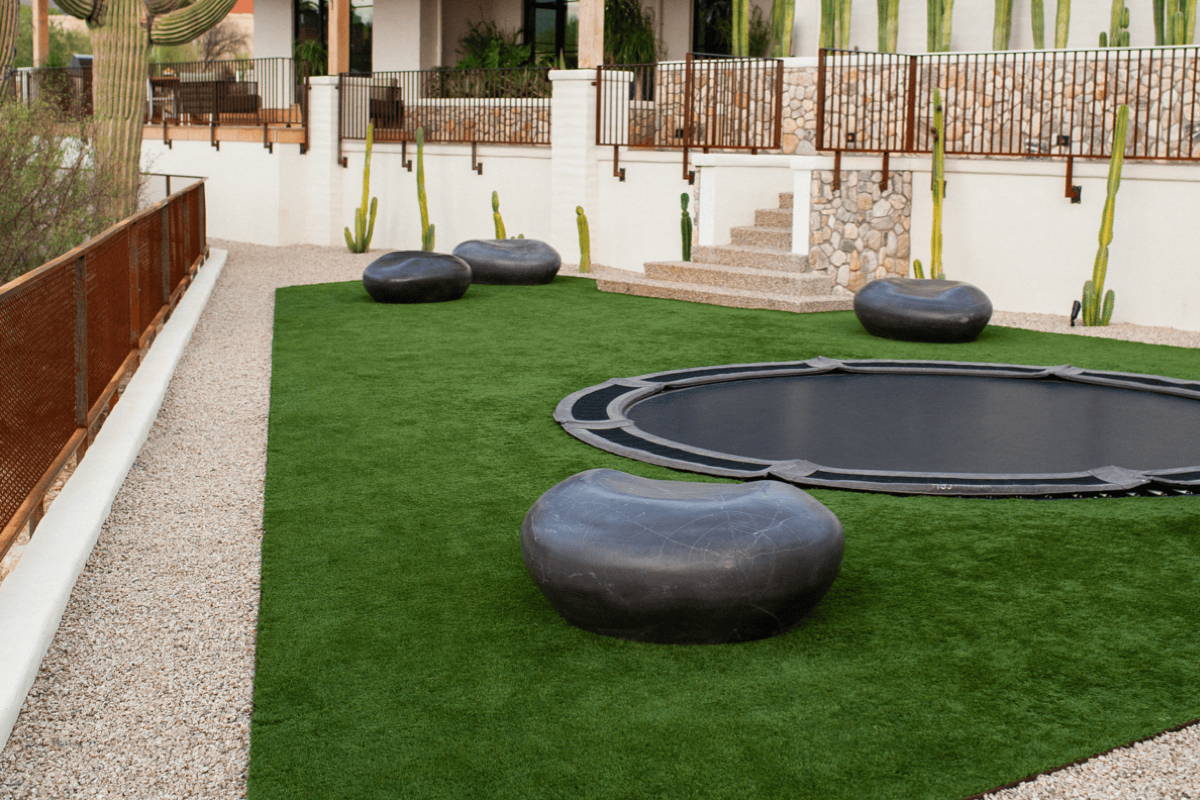 Four black Cast Stone Pebble Garden Seats surrounding an in-ground trampoline on bright green turf.