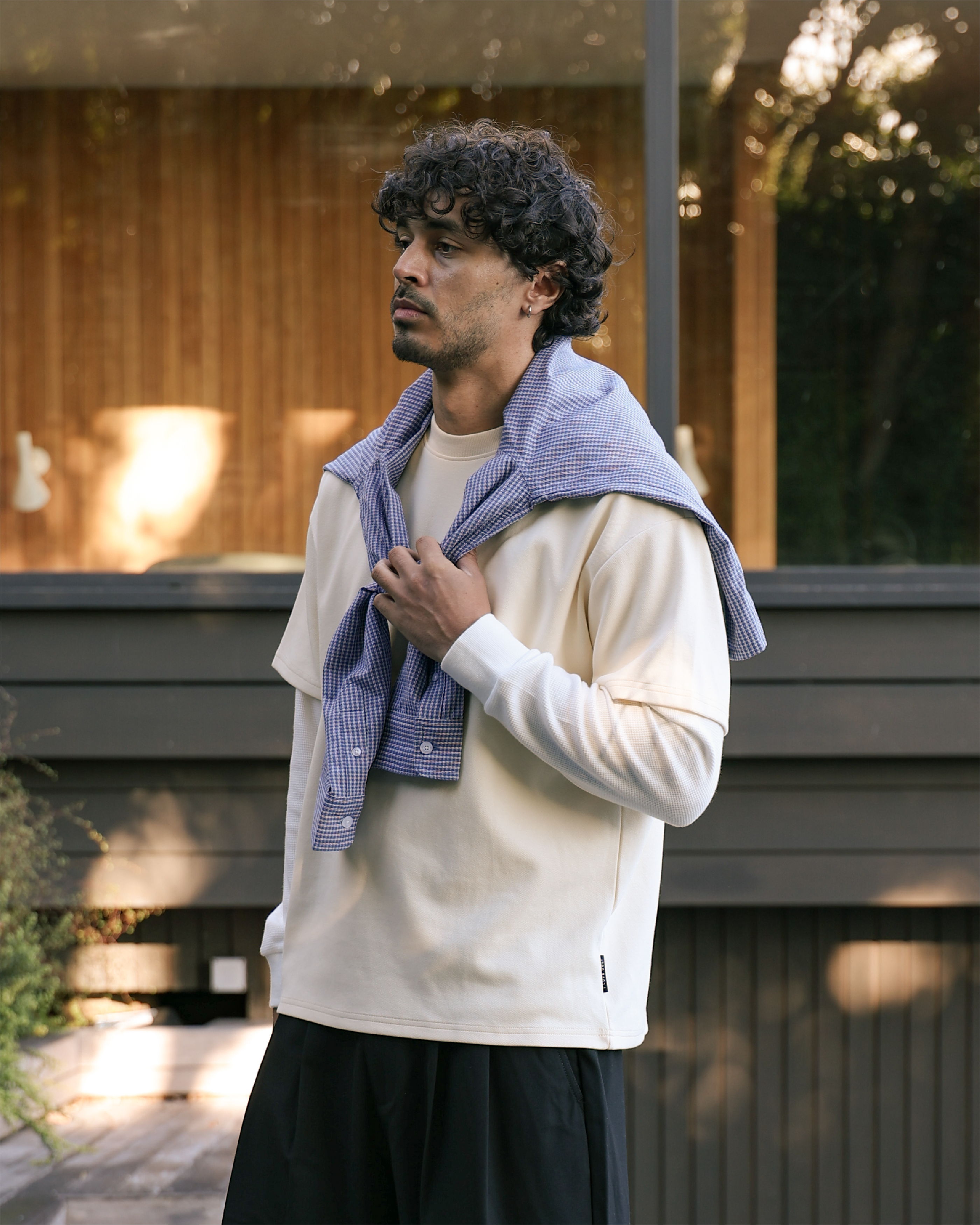 Man wearing a cream shirt and blue sweater draped over shoulders outdoors.