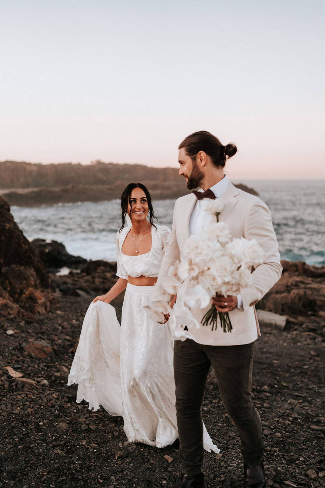 Ellie et James marchent avec leur bouquet sur la plage de Gerringong