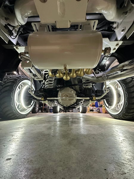 Rear underbody view of white air tank and five gold train horns above white suspension with LED wheel ring lights