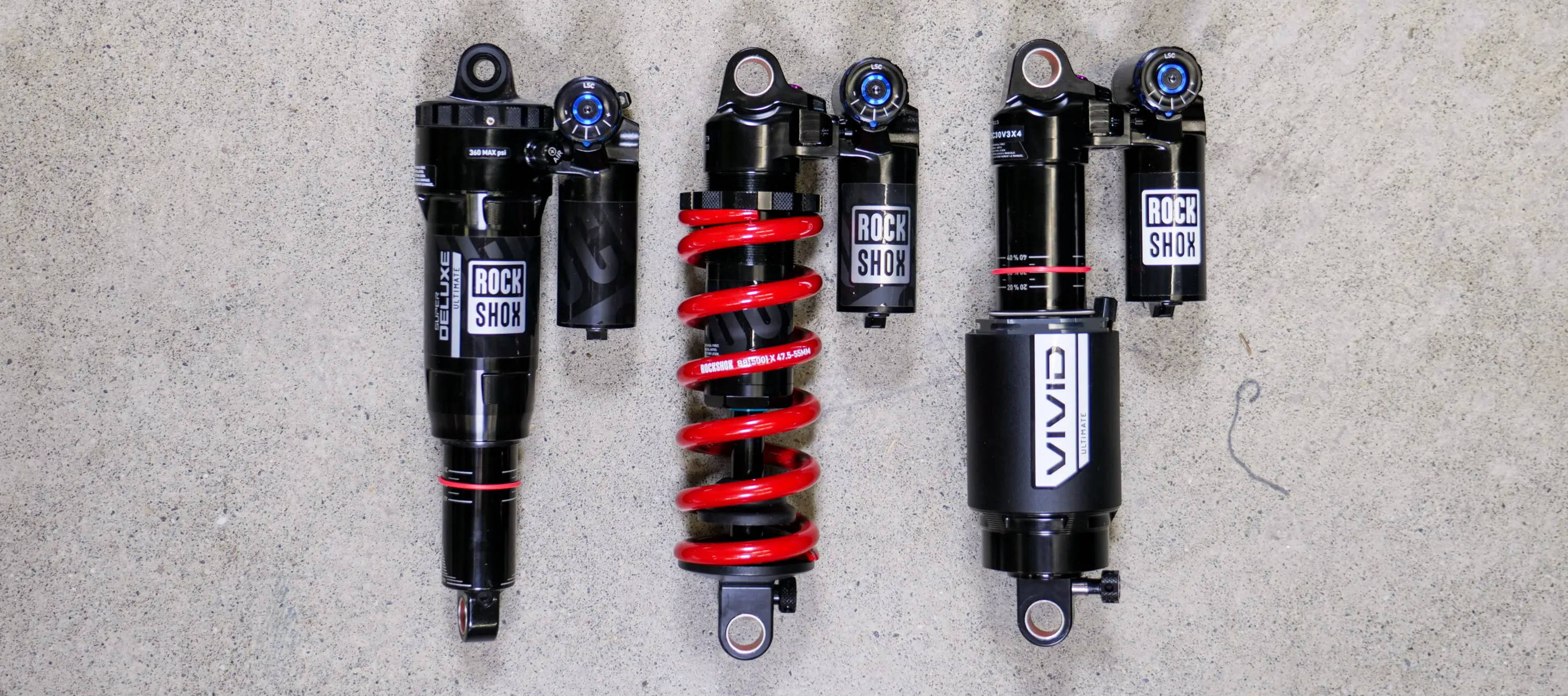 rockshox super deluxe ultimate and super deluxe coil ultimate and vivid rear mountain bike shocks laying on concrete to be compared