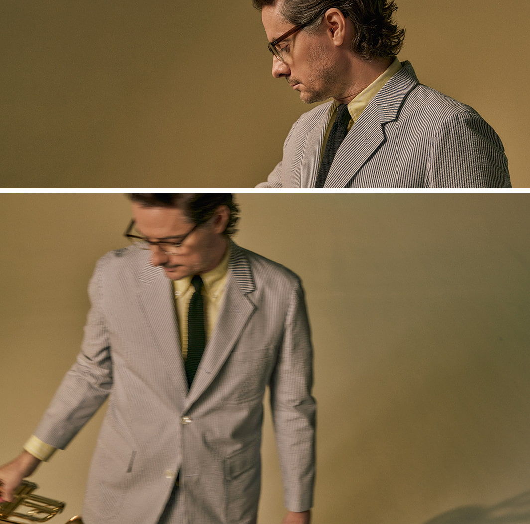 Person in a suit looking down, holding an object against a beige background.