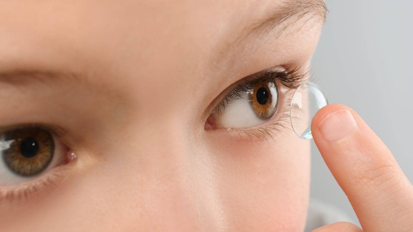  A close-up of a child inserting a contact lens into their left eye.