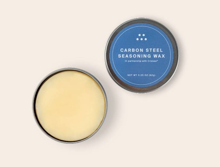 An open tin of Misen Carbon Steel Seasoning Wax seen from above, with beige wax and blue-and-white lid label visible.
