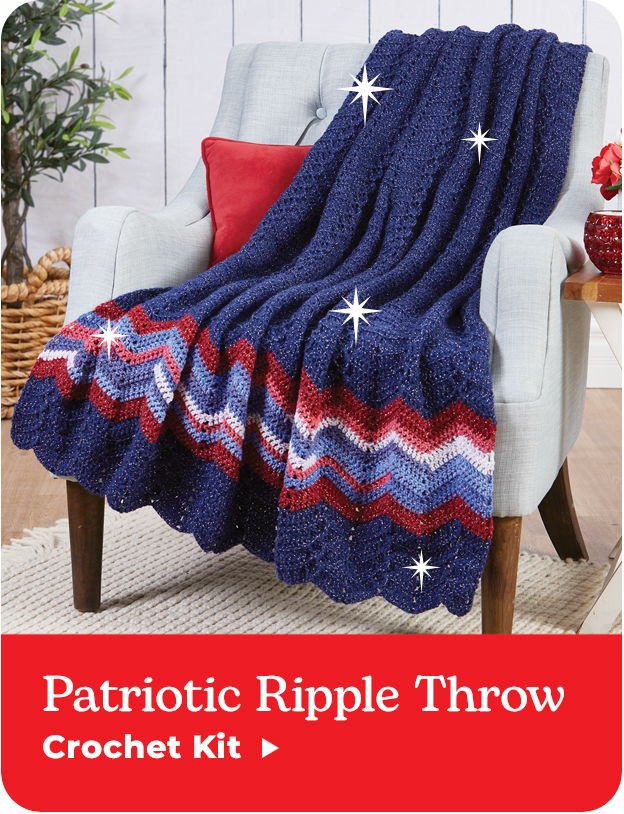 Patriotic Ripple Throw crochet kit on a chair with decorative pillows.